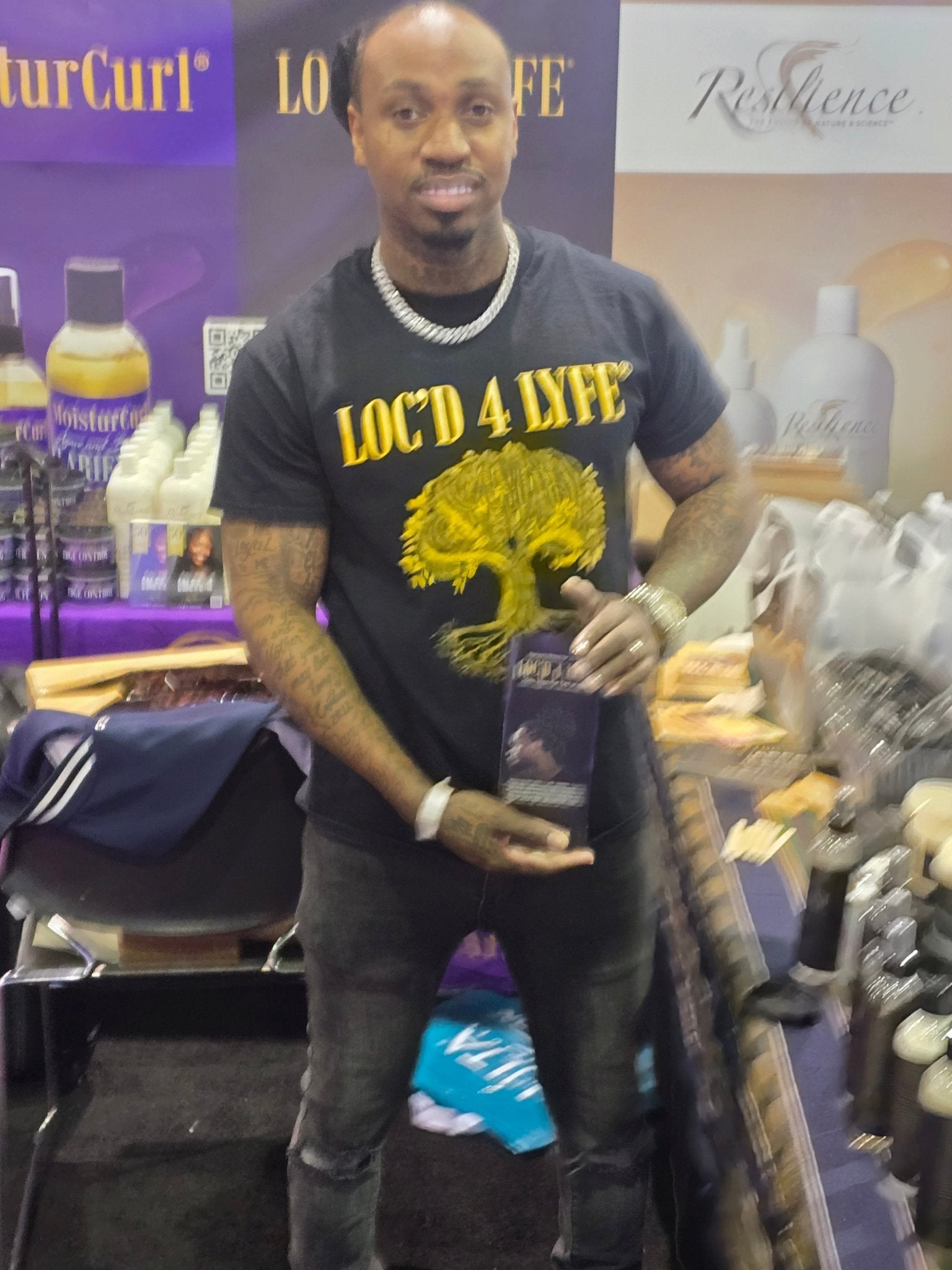 Man in salon holding hair products, wearing LOC'D 4 LYFE T-shirt
